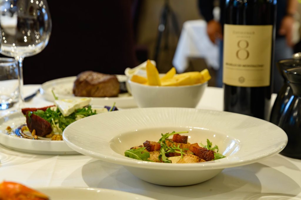 Steak, fries, salads and red wine served at a table at The Gables