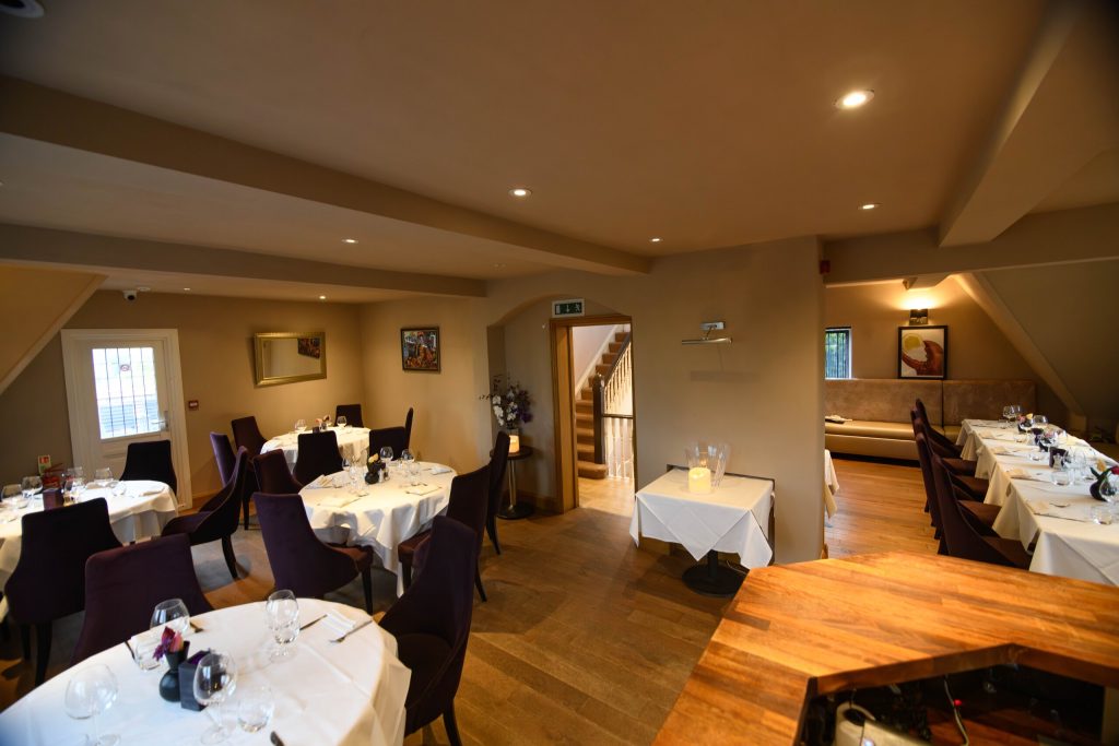 Dining room with round tables laid in white linen and stairs to the first floor at The Gables