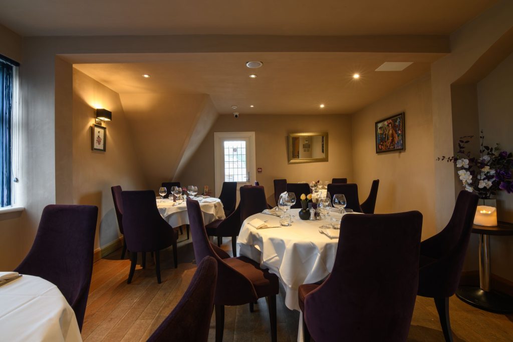 Private dining room at The Gables with purple velvet chairs and tables laid with white linen