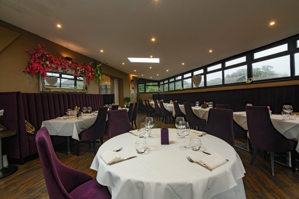 Bright dining room with round tables, purple chairs and long windows at The Gables