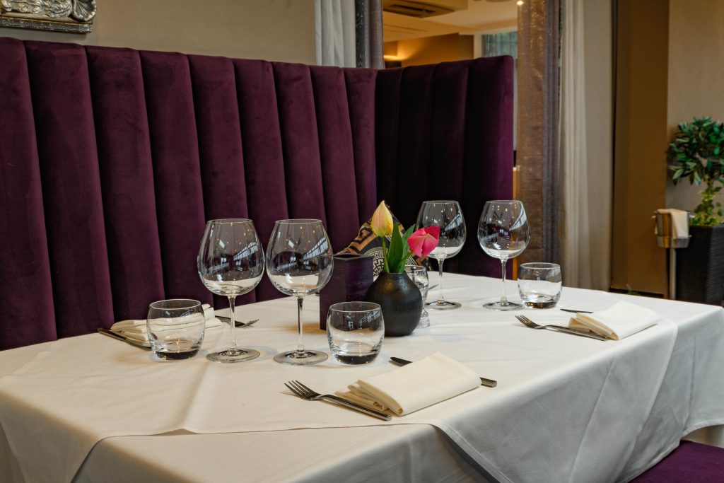 Table set with wine glasses beside a purple velvet booth at The Gables