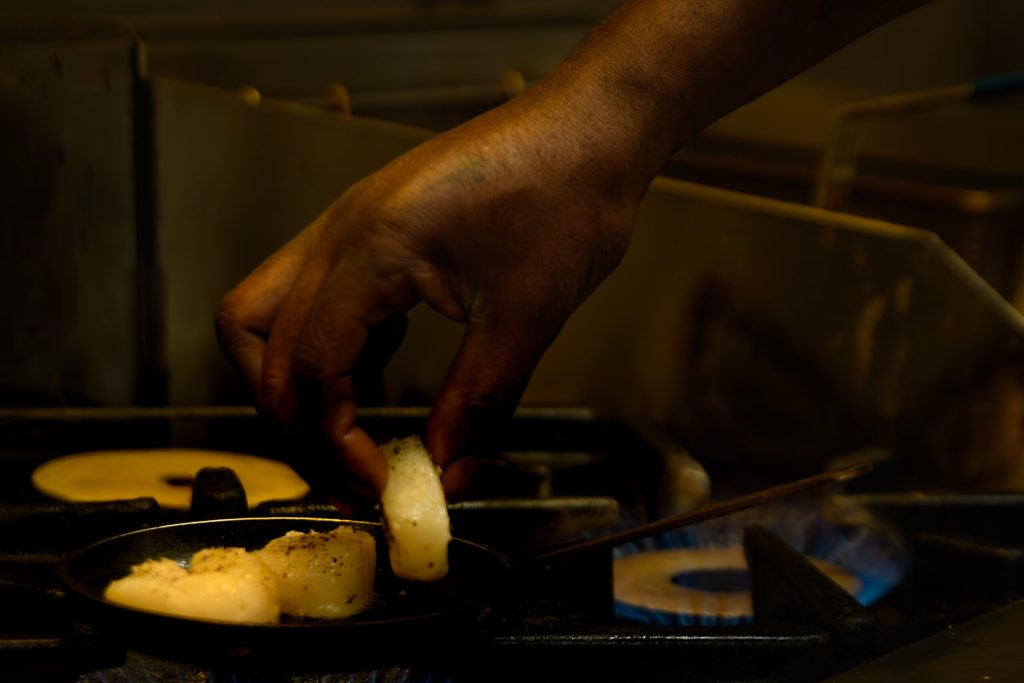 Chef searing food in a pan in the kitchen at The Gables