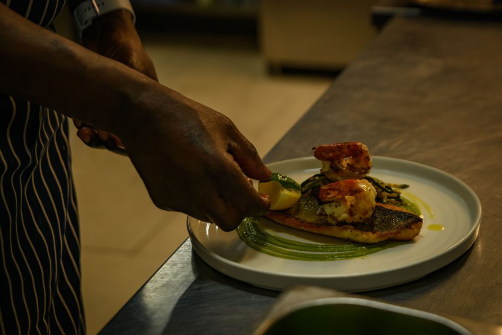 Chef finishing a fish dish topped with king prawns at The Gables